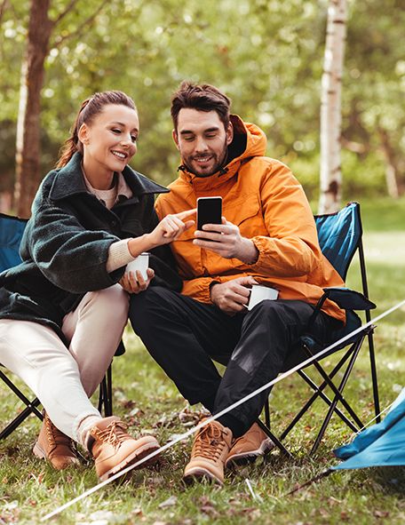 Ein Paar schaut auf ein Smartphone, an einem Zelt sitzend