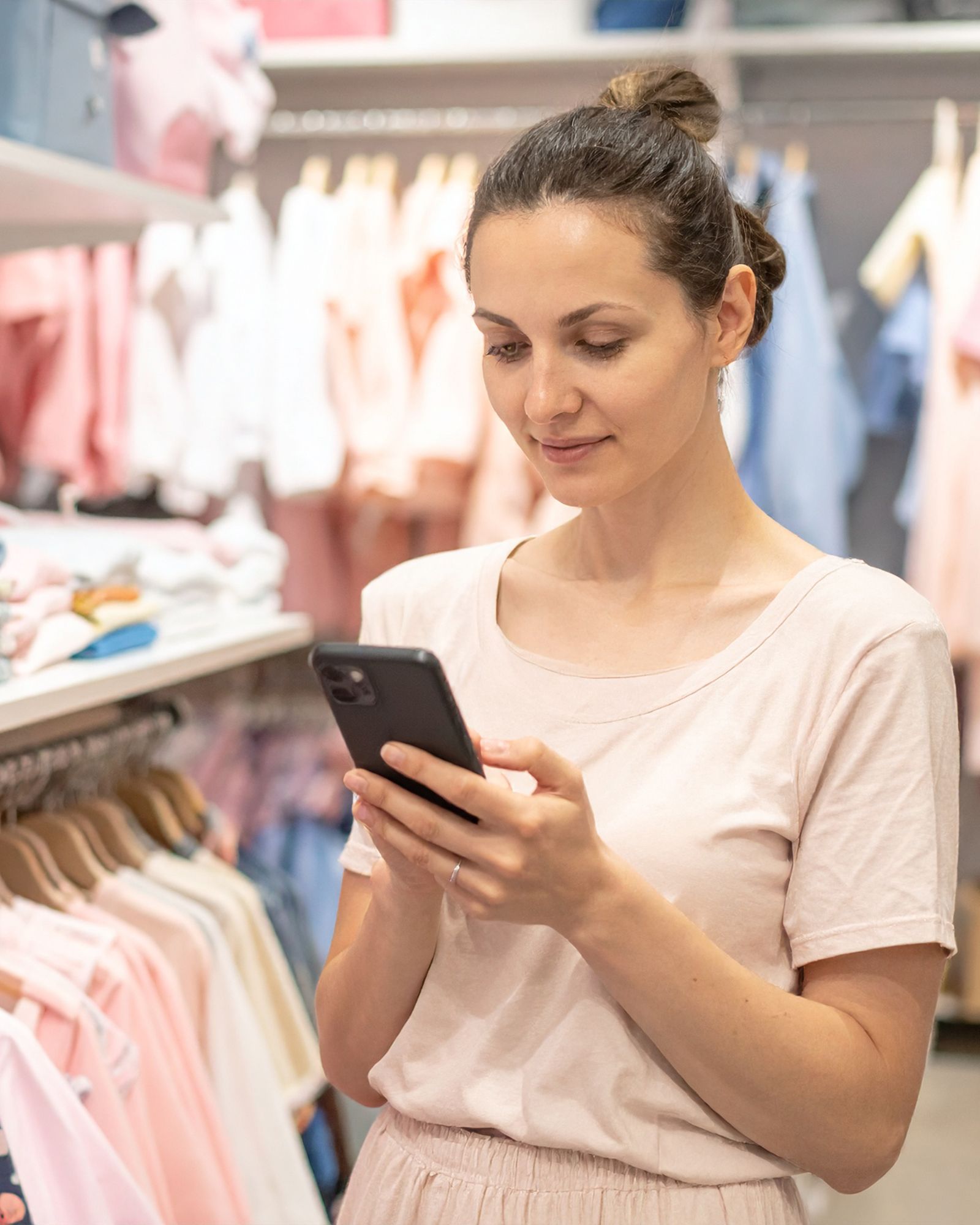 Frau mit Smartphone in einem Shop für Second Hand Kinder-Mode